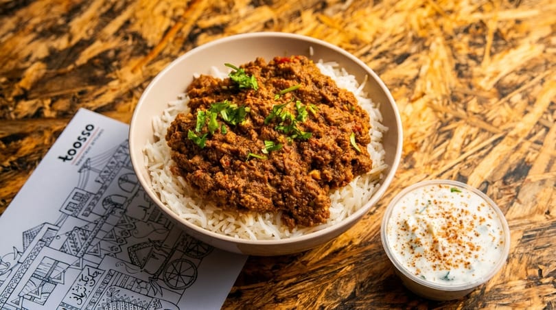 A bowl of Toosso's spiced meat curry over white rice, with a side of raita.