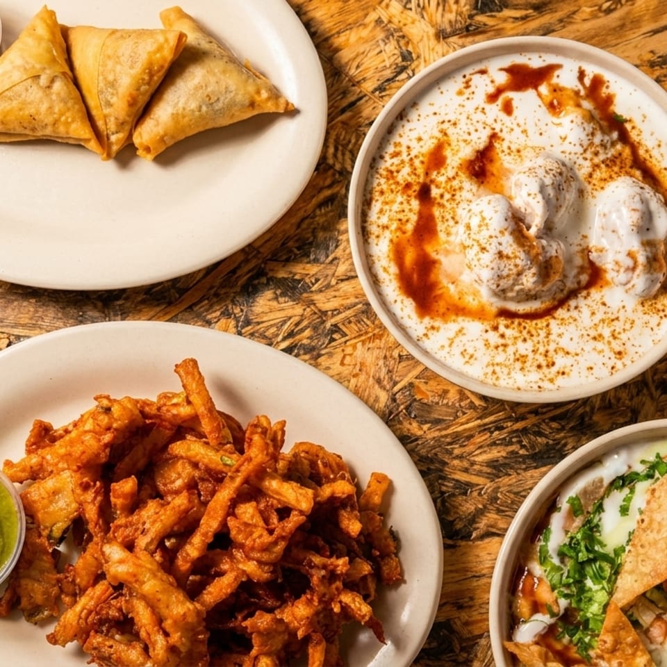 Top-down view of samosas, pakoras, dahi vada, and papri chaat on a rustic wooden table.