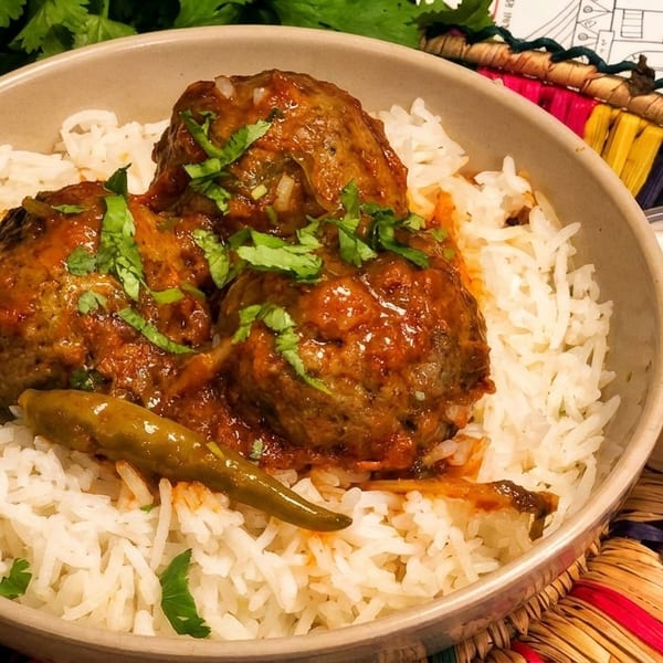 Meatballs in red sauce with cilantro and a green chili, served over white rice with a side of raita.