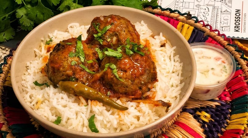 Meatballs in red sauce with cilantro and a green chili, served over white rice with a side of raita.